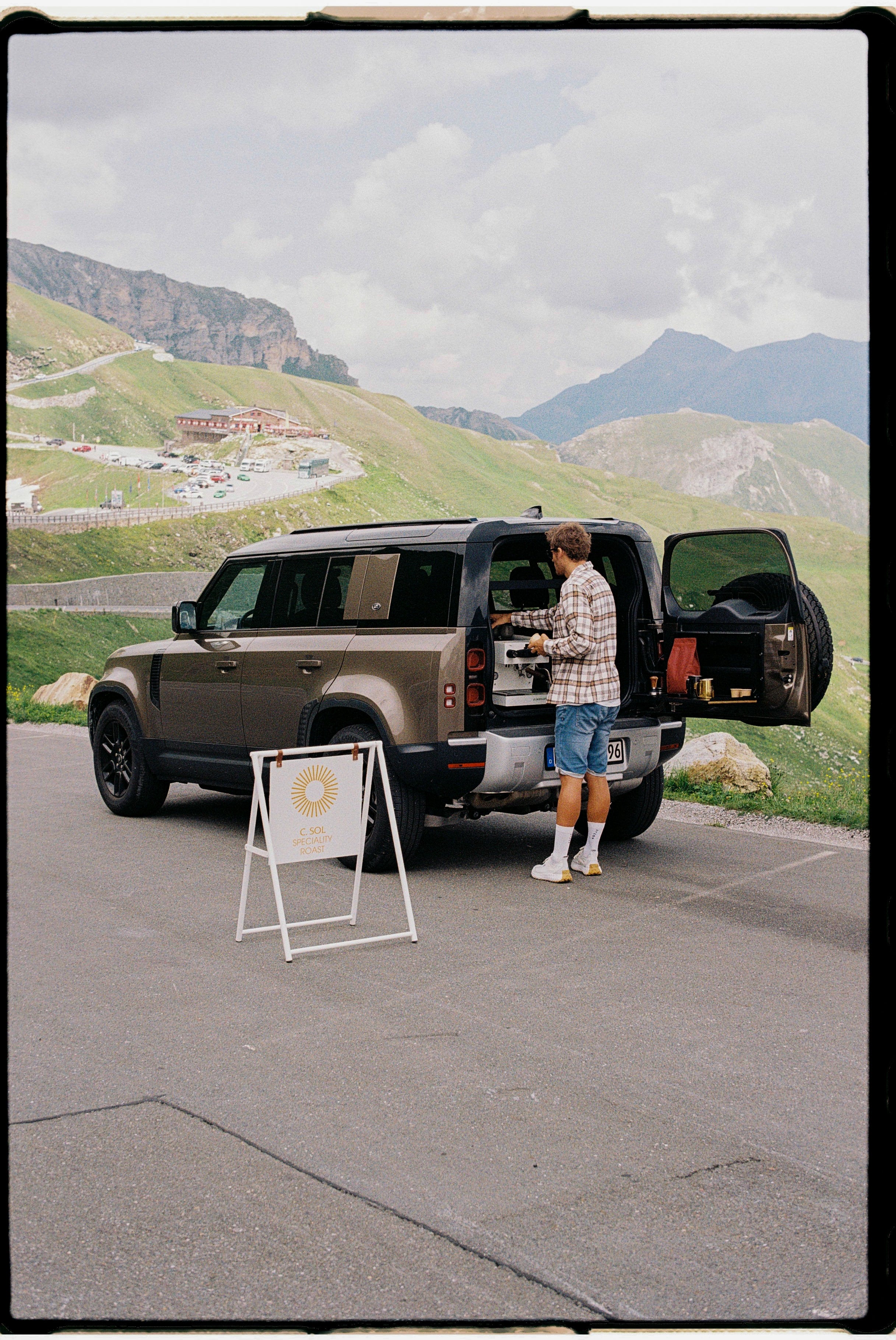 Person standing next to an open SUV door in a scenic mountainous area.
