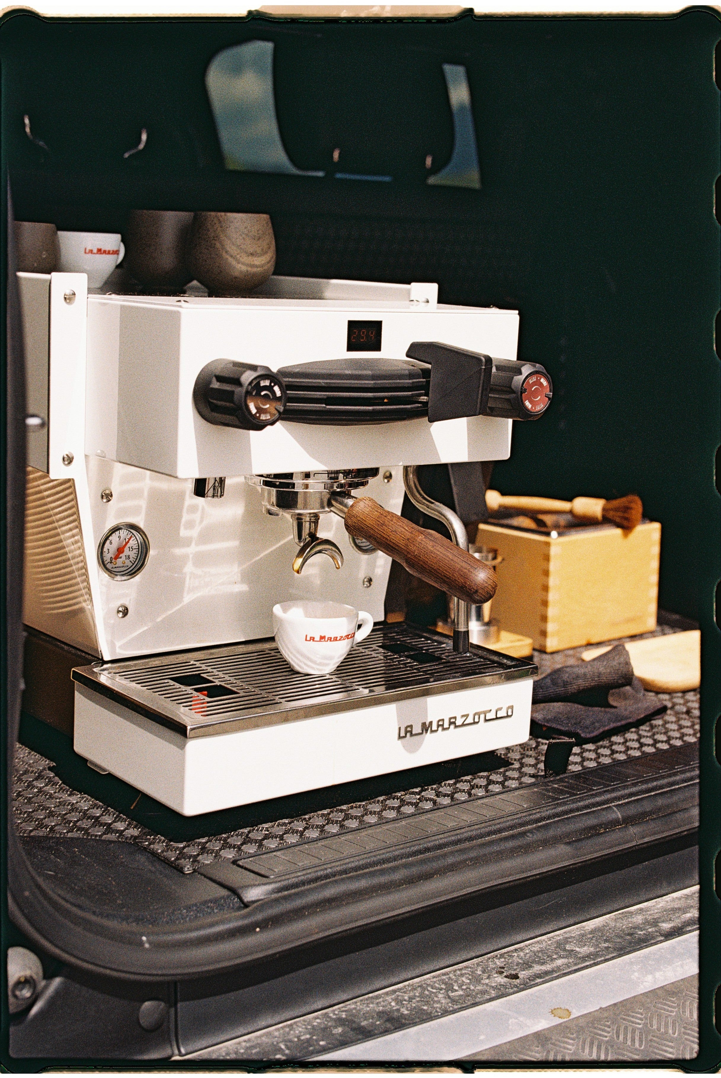 La Marzocco white espresso machine with wooden handle on a dark surface