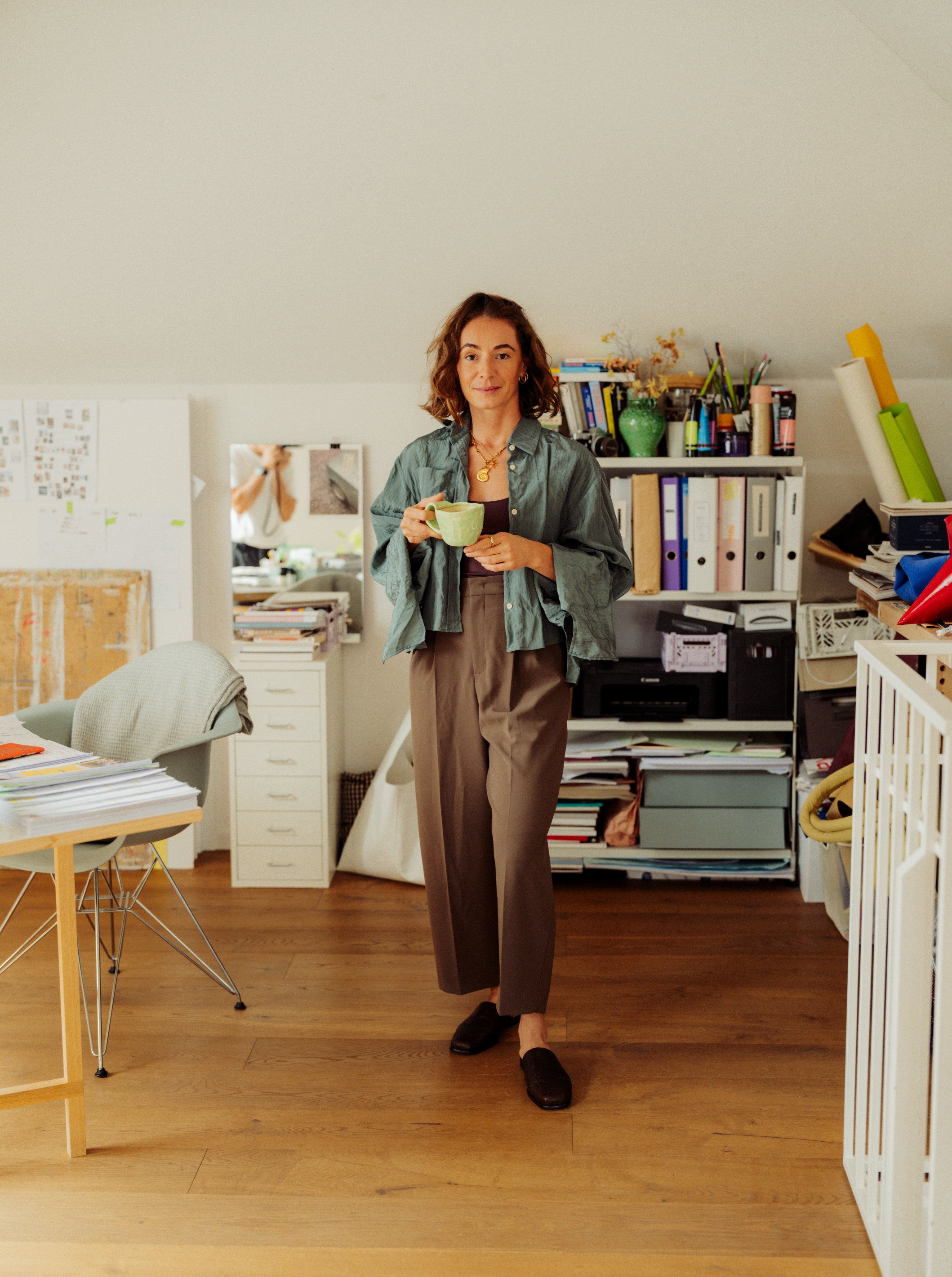 Woman standing in a home office holding a green mug.