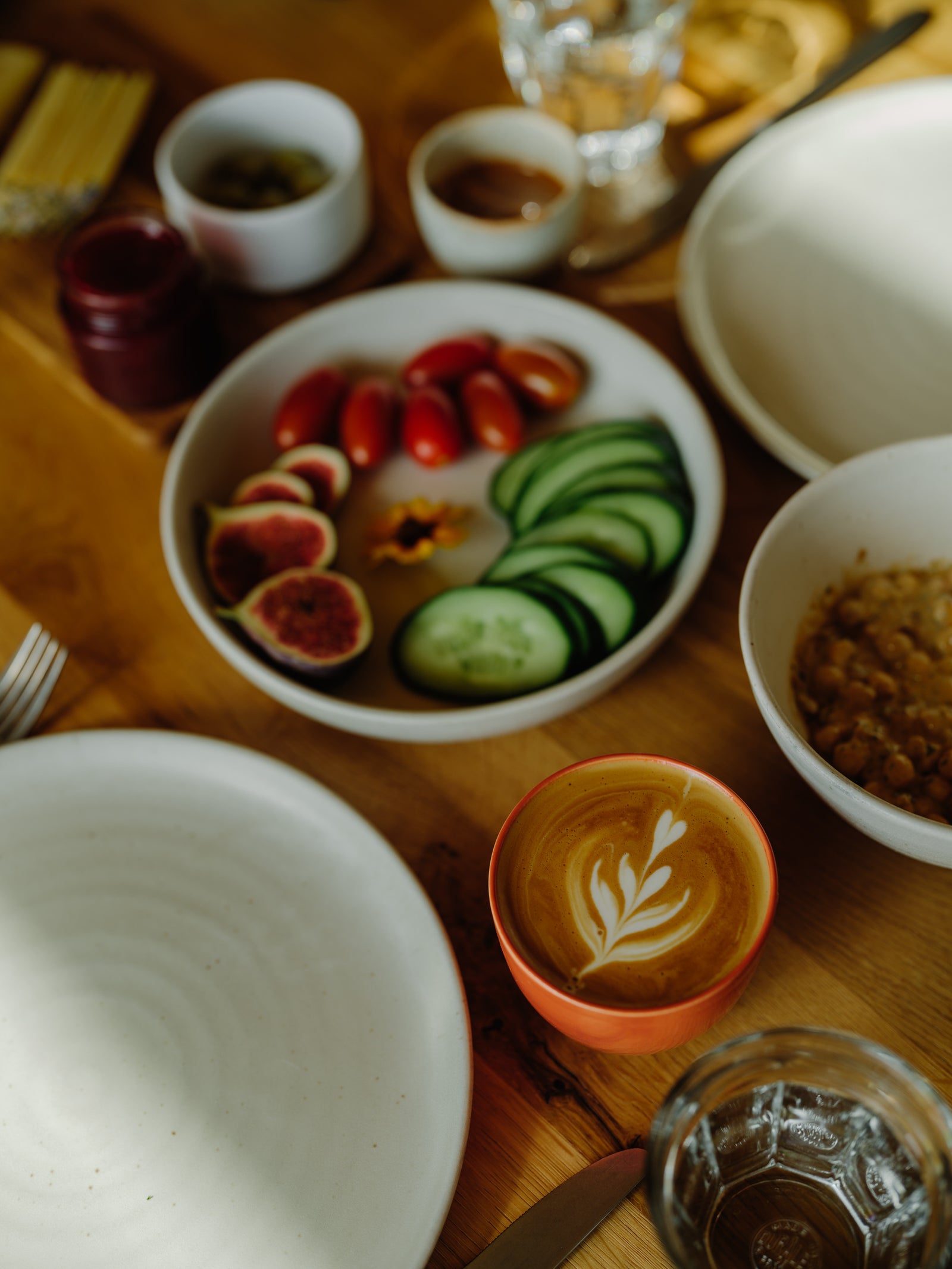 Table setting with a bowl of sliced vegetables, a cup of coffee with latte art, and various dishes.