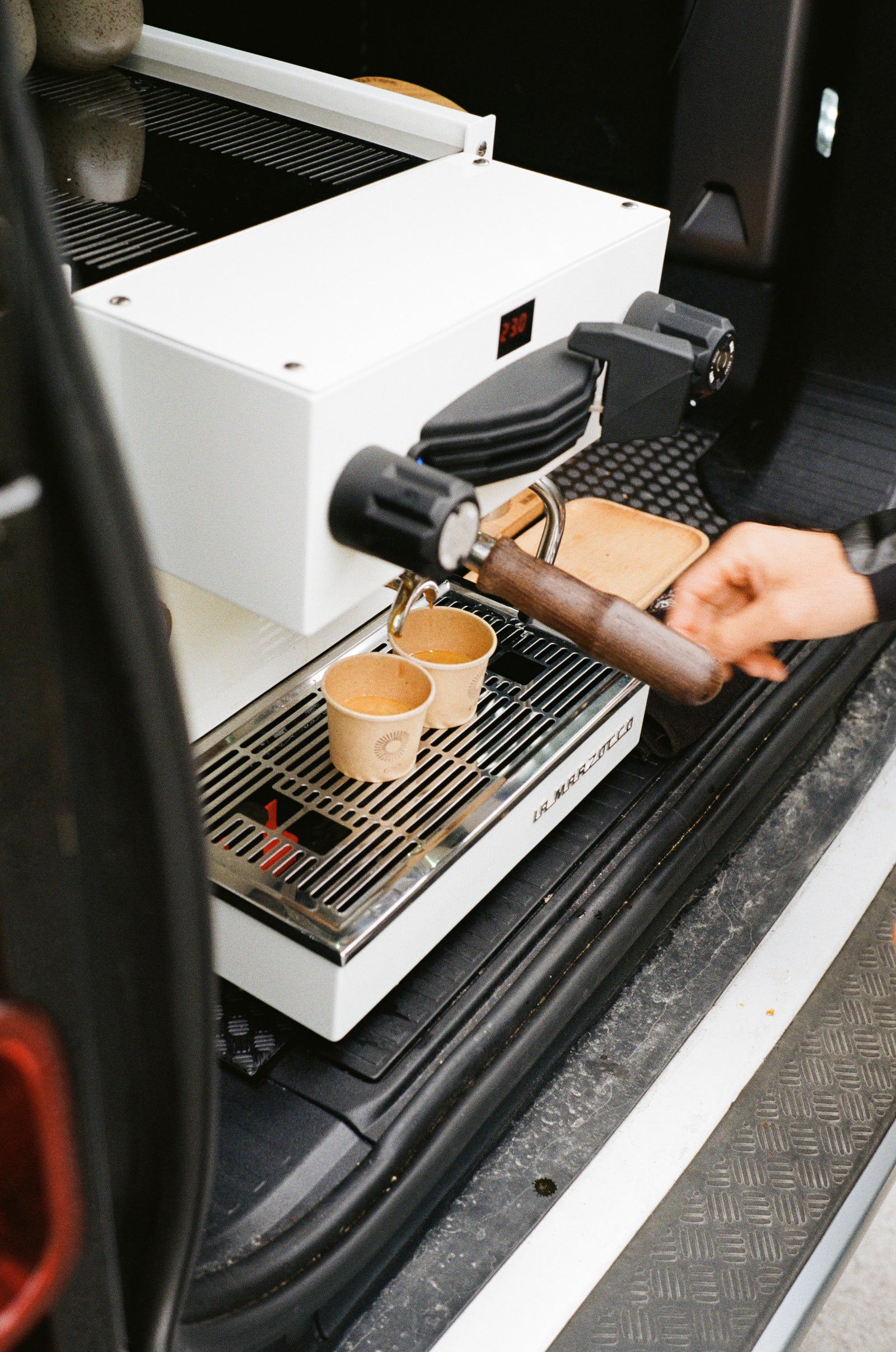 Person using a La Marzocco espresso machine in a vehicle.