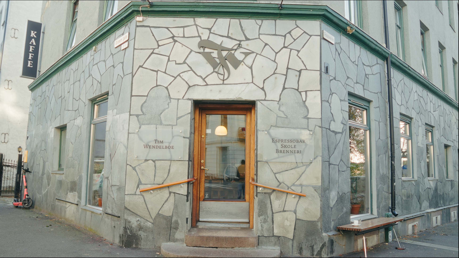 Corner of a building with stone facade and wooden door. Entrance to Tim Wendelboe location