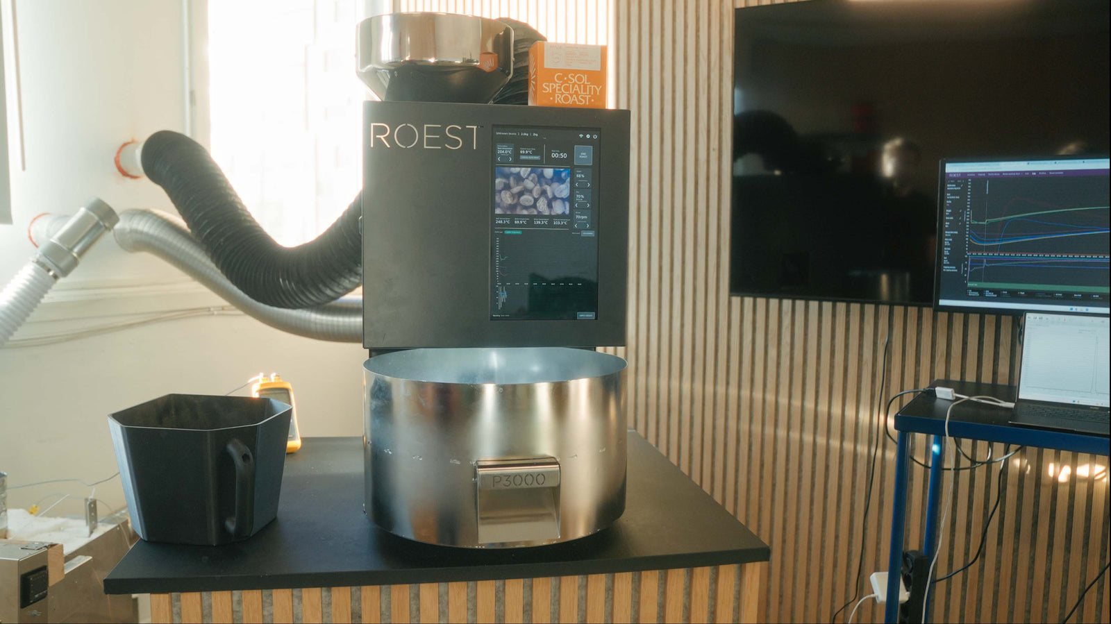 Roest coffee roasting machine on a table with a cup nearby, in a room setting.