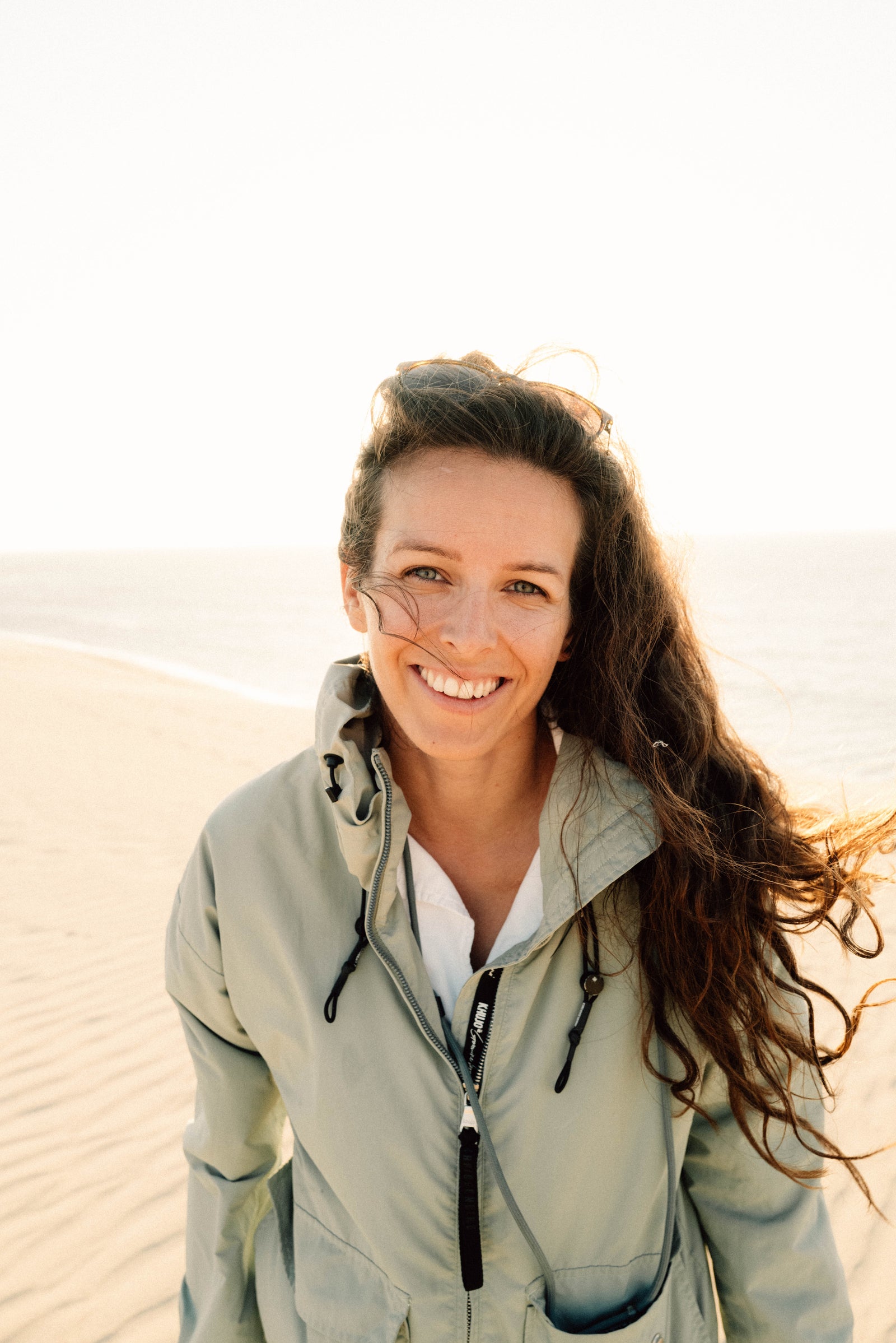 Woman in a light jacket standing on sand dunes with the blurred sea in the background