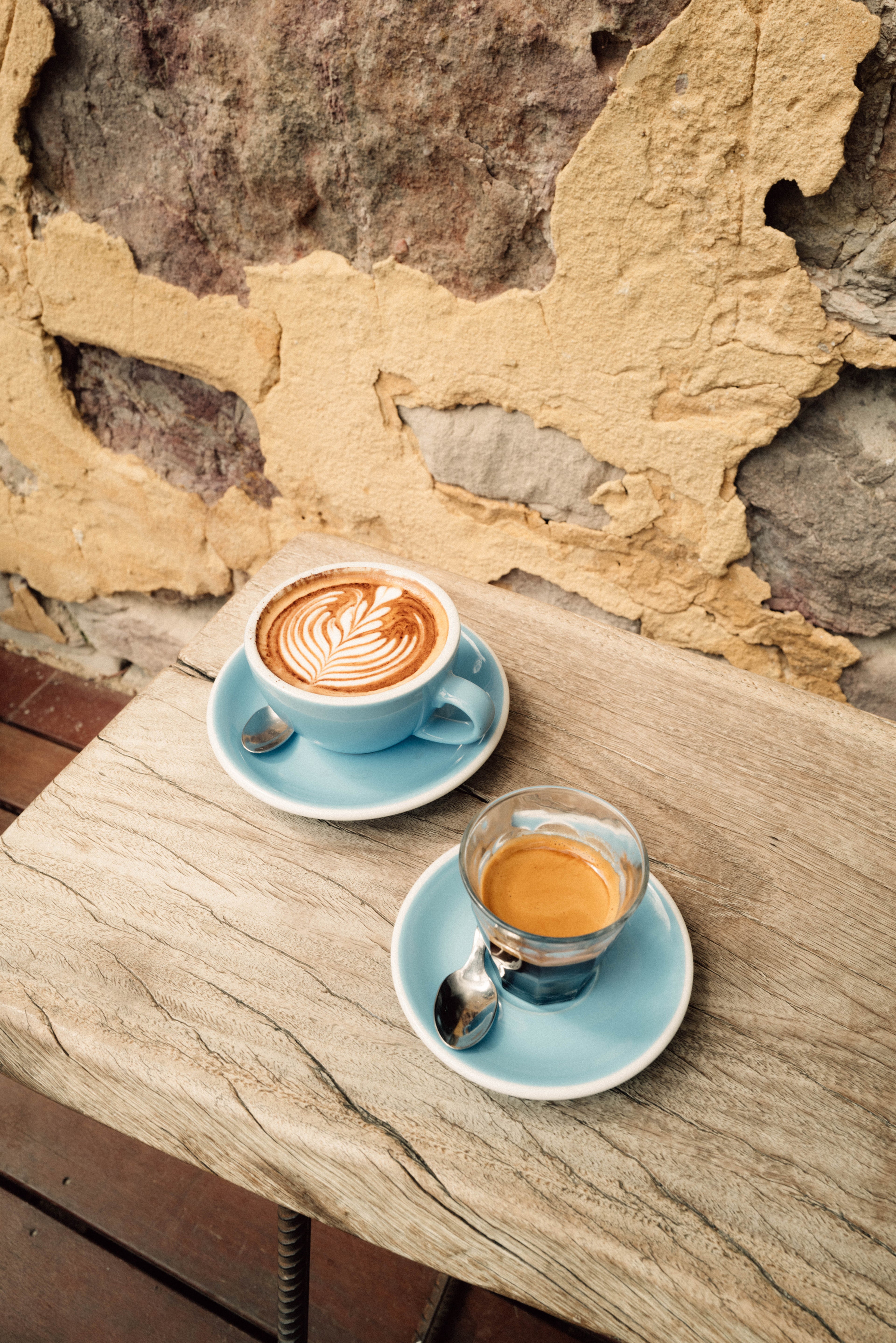 Two cups of coffee on a stone table with a rustic wall background in western australia. One cappuccino, one double espresso