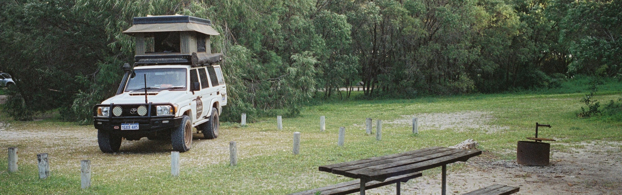 4x4 vehicle with a roof rack parked near a picnic table in a forested area