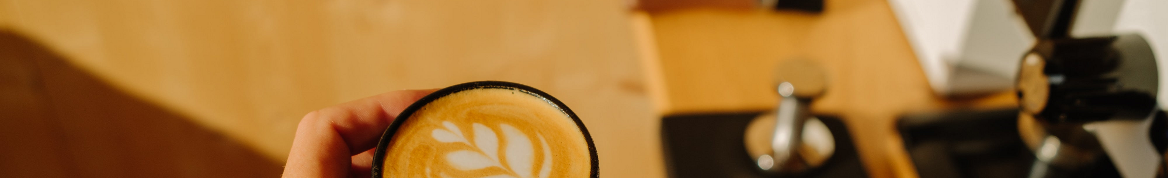 Hand holding a coffee cup with a latte art design on a wooden table.